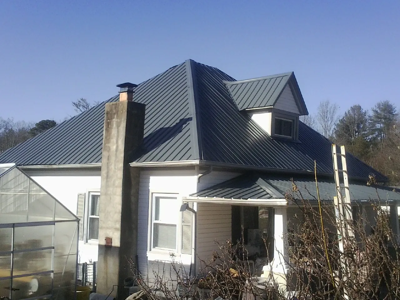Dark blue standing seam metal roof on a white farmhouse with dormer — Slate & Tile Roof Repair by Roofing Brothers in Morganza