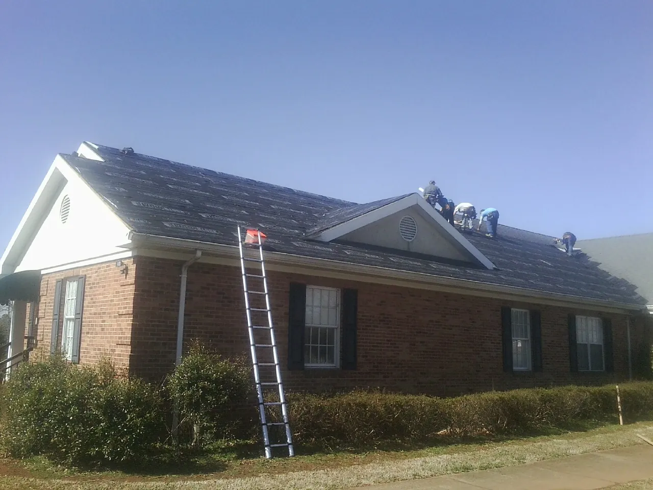 Crew tearing shingles off a brick ranch roof with a ladder set — Metal Roof Repair work by our crew in Morganza