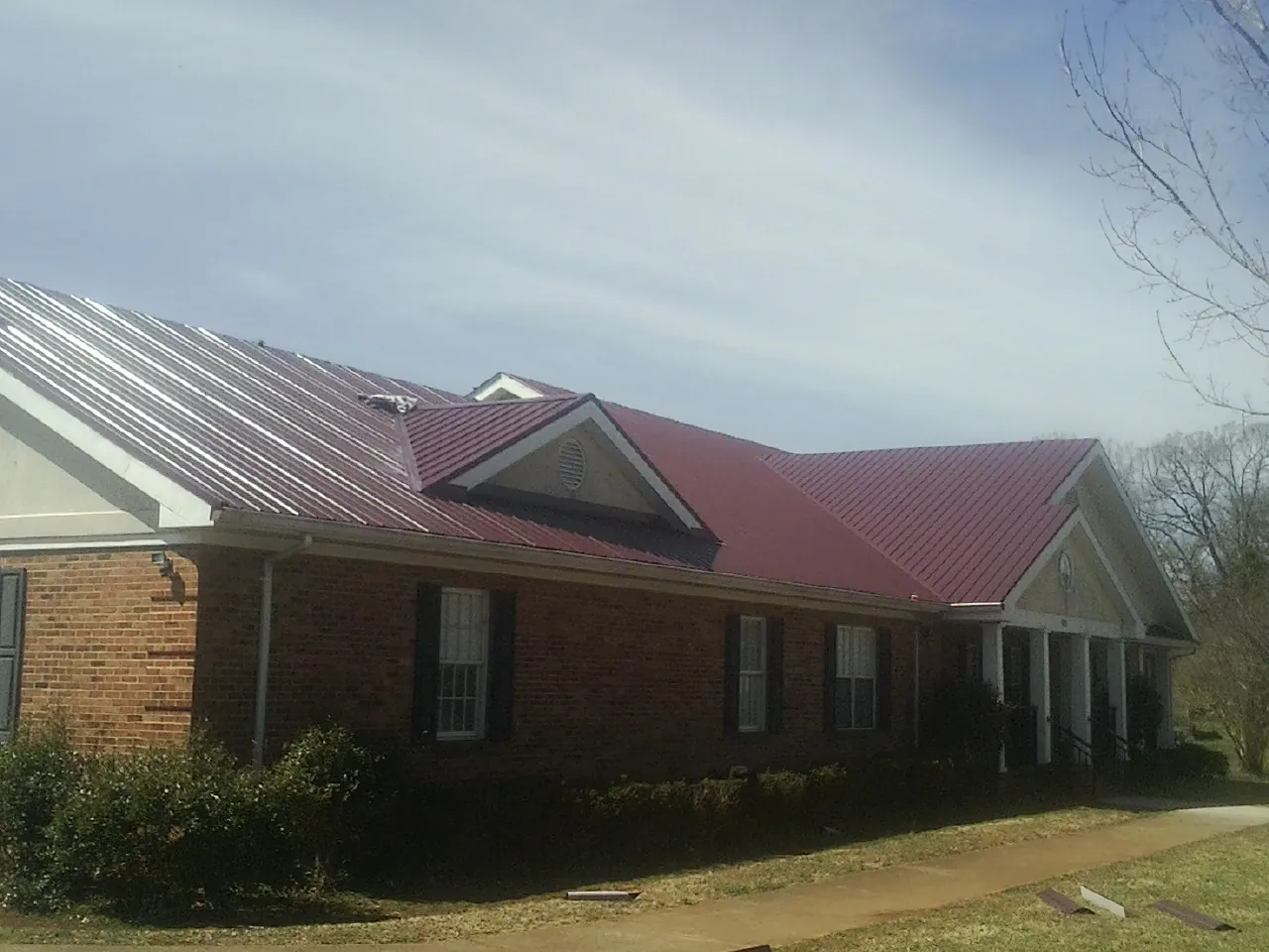 Red metal roof with gabled entries on a long brick building, from a Hail Damage Roof Repair job in Morganza