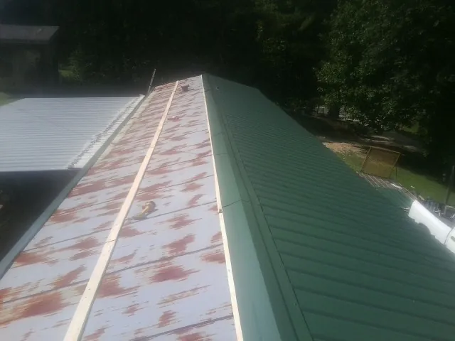 Old rusted panels beside newly installed green metal roofing — Wind Damage Roof Repair by Roofing Brothers in Morganza