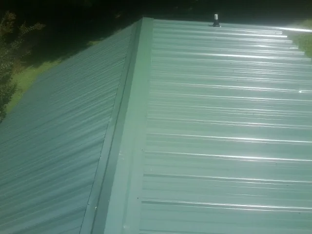 New green metal panels meeting at the ridge of a roof — Flat Roof Repair work by our crew in Morganza