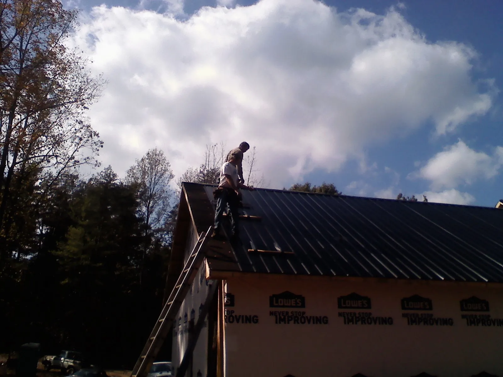 Roofer fastening dark metal panels high against a cloudy sky, from a Roof Inspection job in Morganza