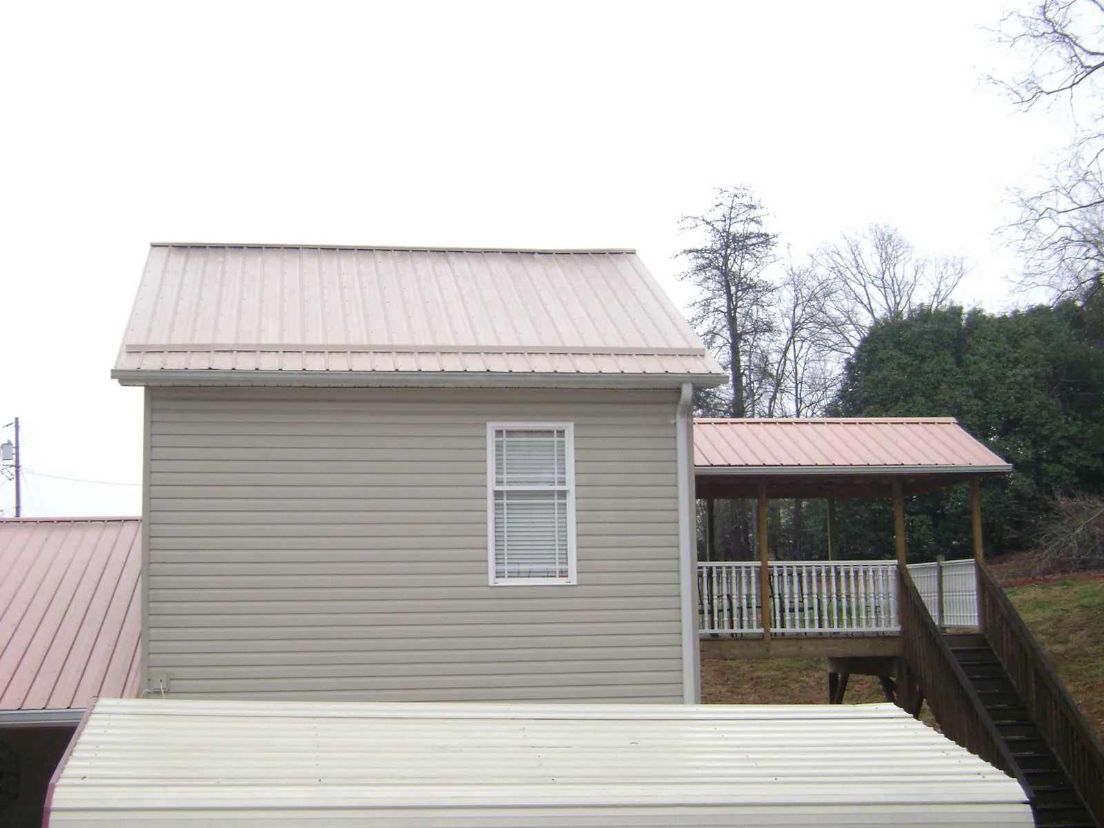 Tan metal roofs on a two story addition and attached porch, from a Roof Replacement job in Morganza